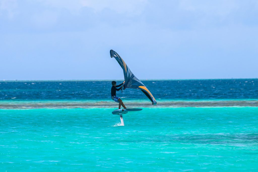 A young surfer wingfoiling on vibrant turquoise ocean waters, showcasing water sports and adventure.